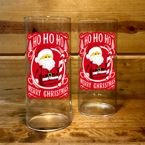 Two clear glasses with Santa Claus design and 'Ho Ho Ho Merry Christmas' text on a wooden background. 2.5" x 6" inches